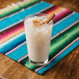 A tall glass of horchata over ice, dusted with cinnamon and with a cinnamon stick.