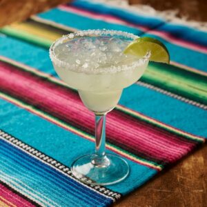 A margarita in a stemmed glass with a coarse salt rim and a lime wedge.